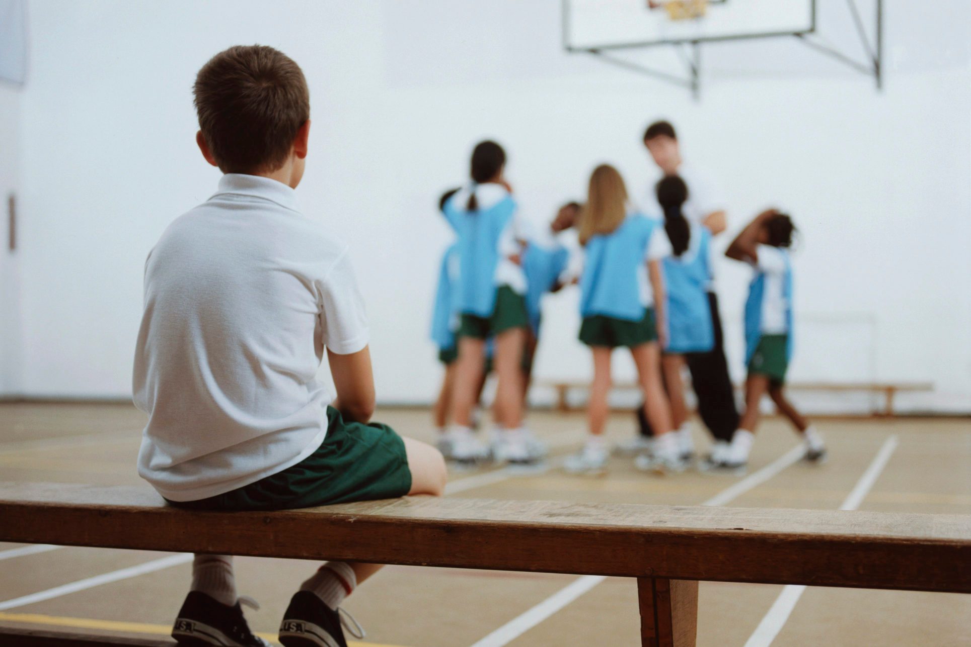 young boy sitting on bench watching basketball team play