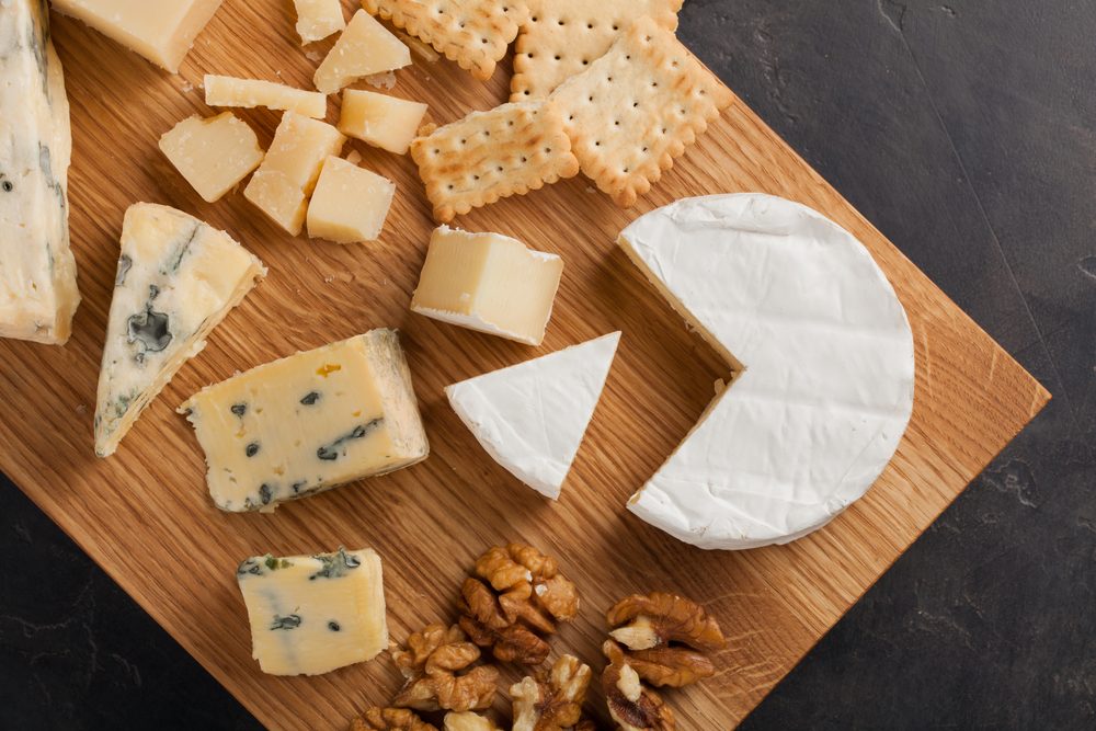 Tasting cheese dish on a wooden plate. Food for wine and romantic, cheese delicatessen on a dark stone table. Top view.