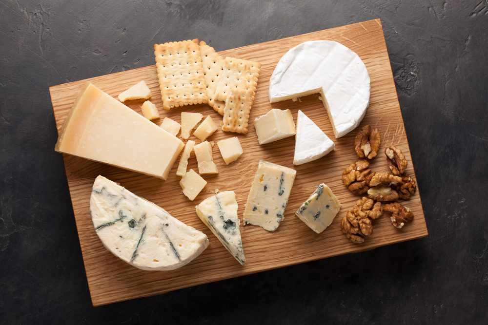 Tasting cheese dish on a wooden plate. Food for wine and romantic, cheese delicatessen on a dark stone table. Top view.