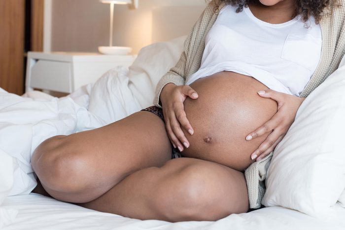 pregnant woman sitting on bed holding her belly