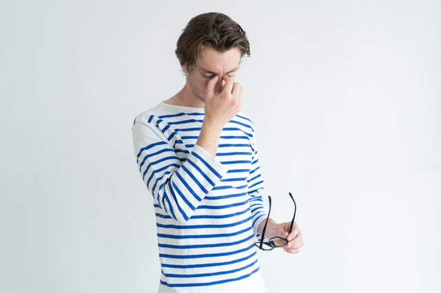Exhausted man rubbing bridge of nose while feeling eye fatigue. Tired young male manager massaging nose and holding glasses. Tension concept