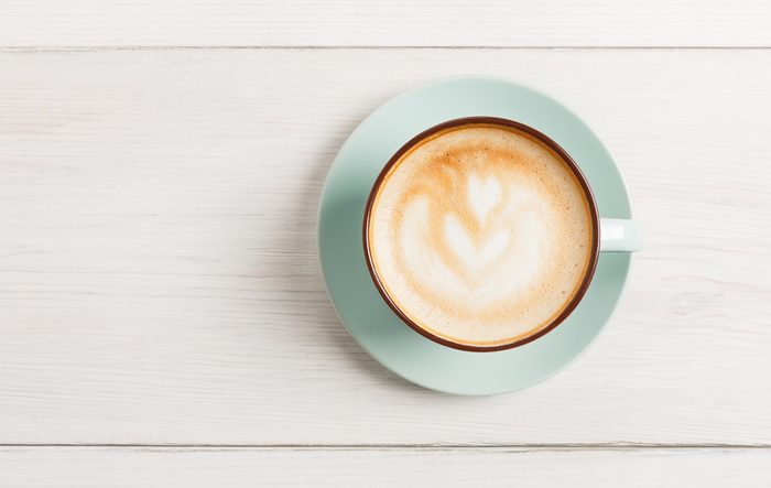 Cappuccino with frothy foam, blue coffee cup top view closeup on white wood background with copy space. Cafe and bar, barista art concept.