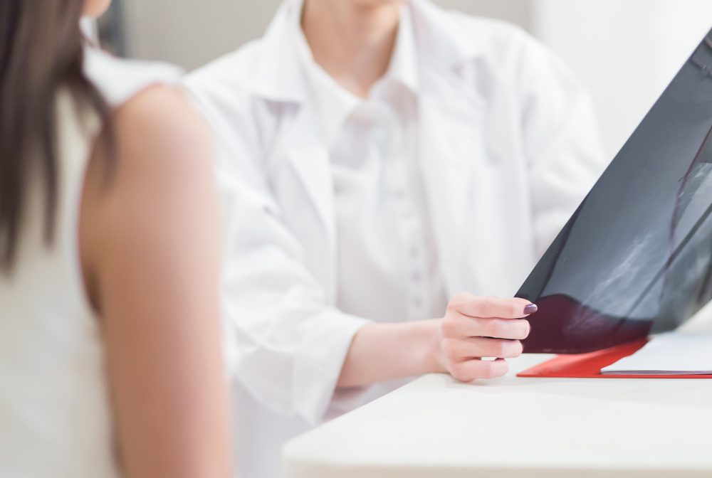 Female doctor holding the Mammogram film image and give advice her patient in consulting room.