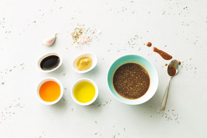 Homemade salad dressing and ingredients, including balsamic vinegar, honey, olive oil, mustard, garlic, and salt. 