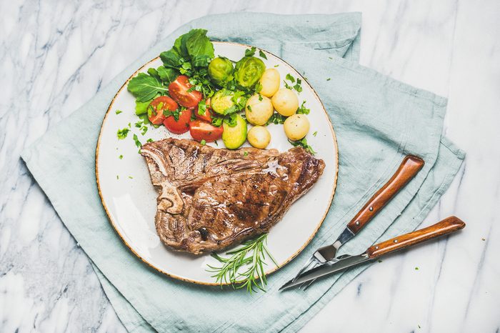 Grilled steak with vegetables and fresh rosemary on a plate.