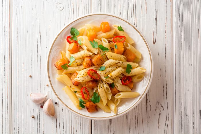 Penne pasta with pumpkin, chilli and parsley in plate on white wooden background. Top view.