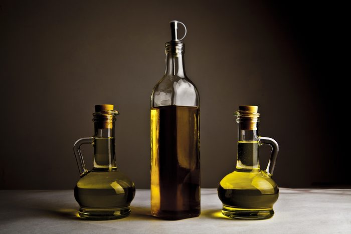 Backdrop of three olive oil glass transparent bottle with cork stand on white table on kitchen space room, on dark black background Empty space for inscription