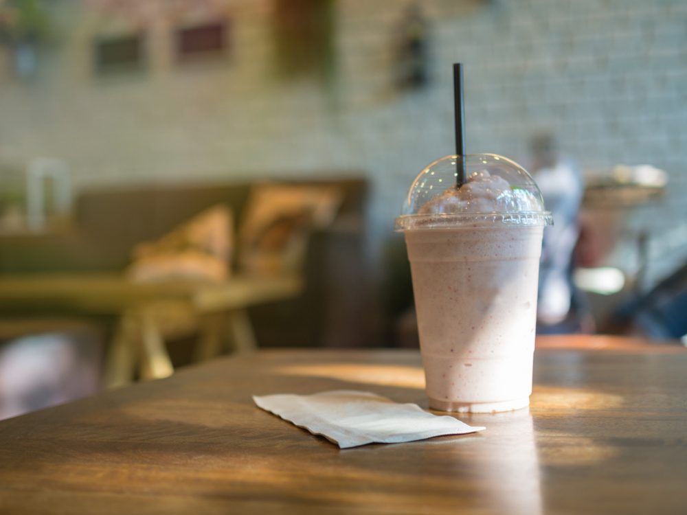 Smoothie with straw in plastic cup on table