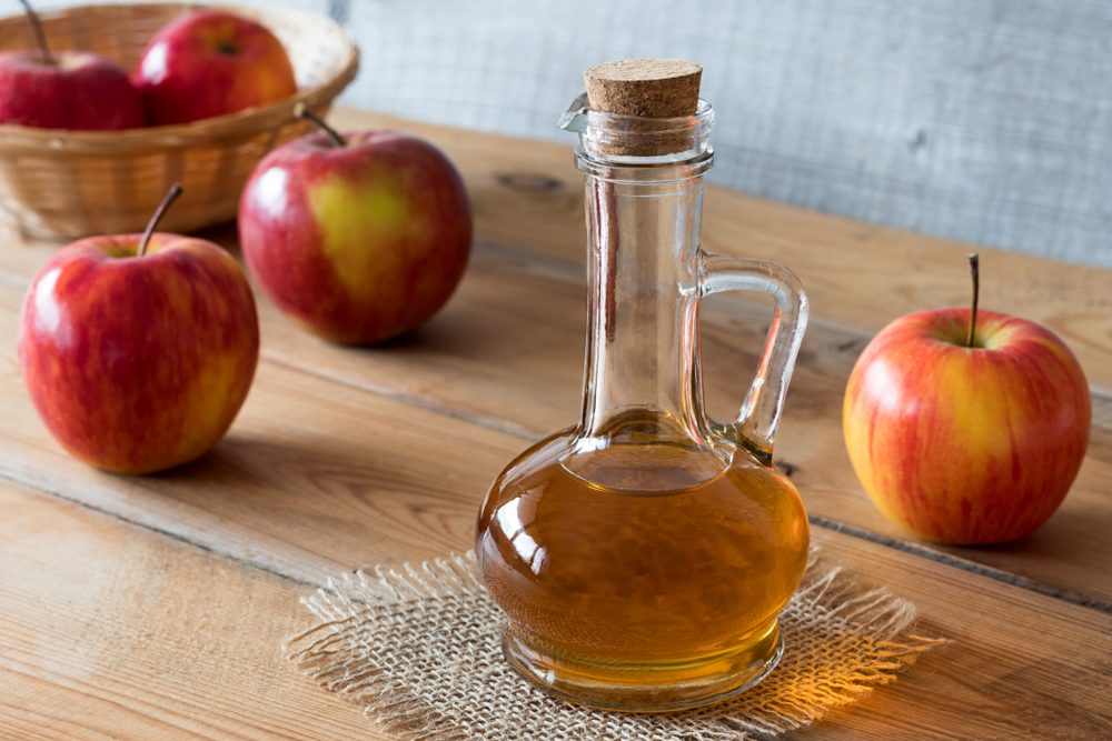 A bottle of apple cider vinegar on a wooden table, with apples in the background