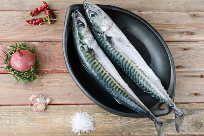 Two fresh mackerels in a black serving bowl with condiments