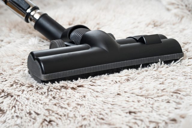 Close up of the head of a modern vacuum cleaner being used while vacuuming a thick pile white carpet.still life dark tone.