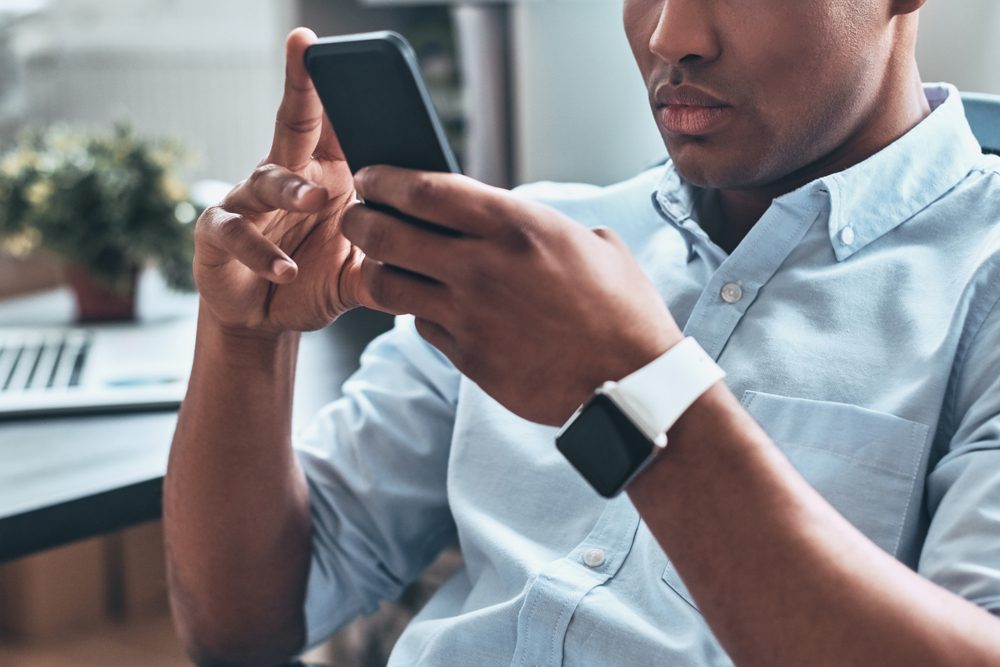 Typing business message. Thoughtful young African man using smart phone while sitting in the office