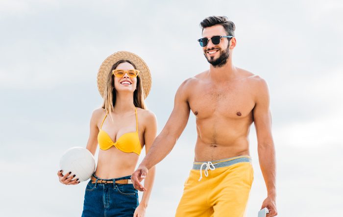 beautiful young couple in beach clothes with volleyball ball in front of cloudy sky