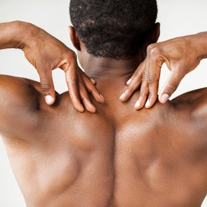 Muscular black man. Rear view of young muscular black man touching his shoulders while standing isolated on grey background