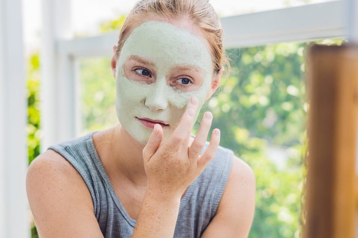 Spa Woman applying Facial green clay Mask. Beauty Treatments. Close-up portrait of beautiful girl applying facial mask.