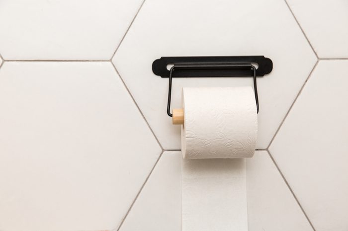 A white roll of soft toilet paper hanging on a modern chrome holder on a light bathroom wall.