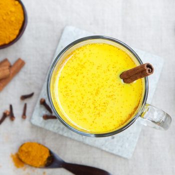 Turmeric drink, latte, tea, milk with cinnamon in a glass mug with fresh and dried turmeric on a textile grey background. Top view. Copy space.