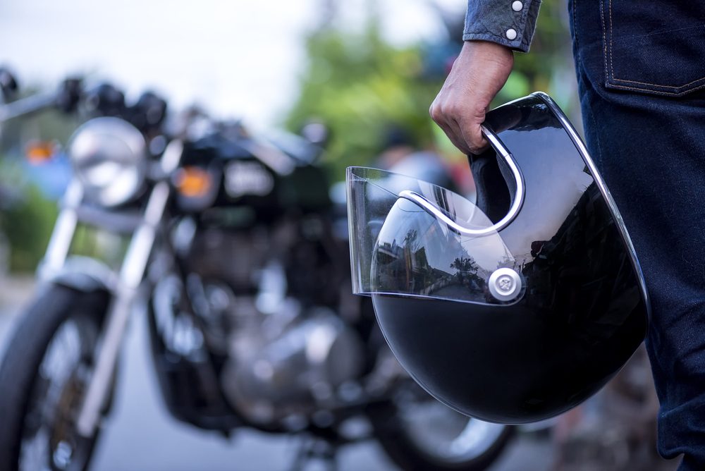 Handsome man in jean is holding a helmet and vintage motorcycle blur background