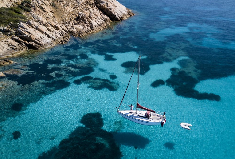 Aerial view of a boat in front of the Mortorio island in Sardinia. Amazing beach with a turquoise and transparent sea. Emerald Coast, Sardinia, Italy.