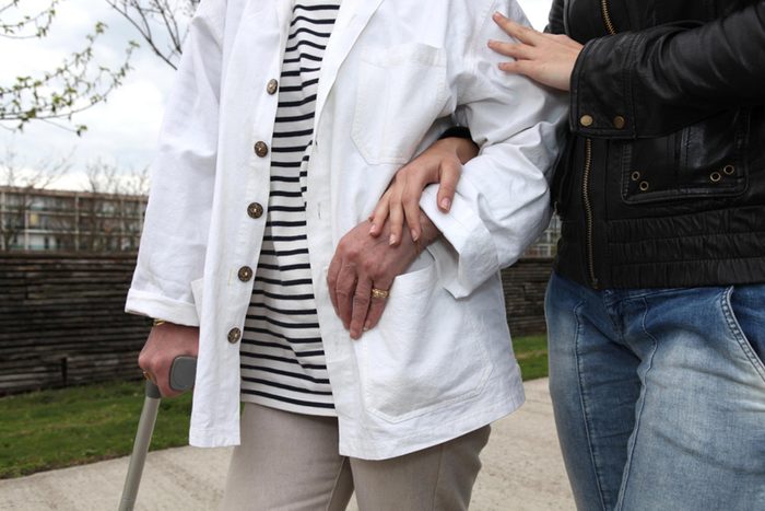 older woman walking with cane with help from friend