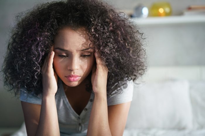 Lonely young latina woman sitting on bed. Depressed hispanic girl at home, looking away with sad expression.