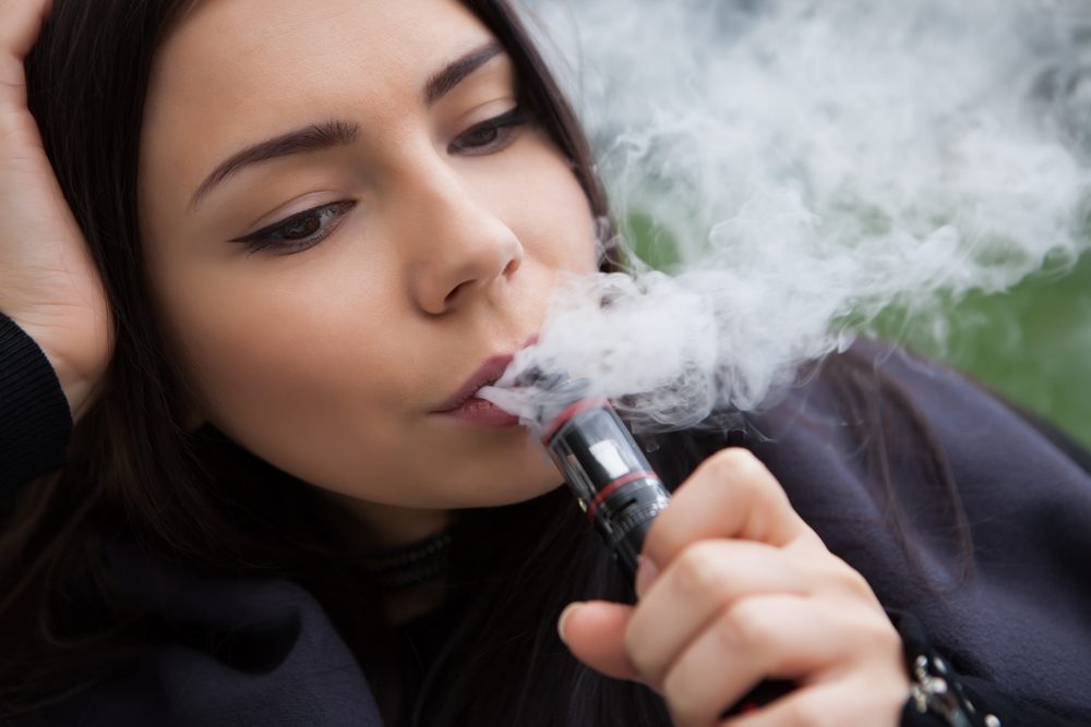 Quit smoking nicotine,start vaping e-juice.Pretty young woman using vaporizer device to smoke vape.Portrait of beautiful brunette girl smoking ecig