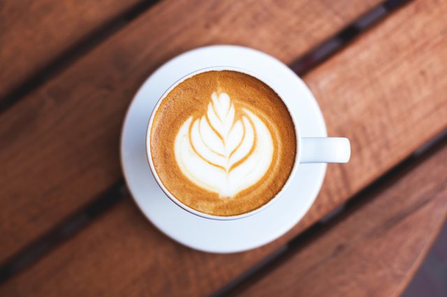 A cup of coffe with latte art on wooden table. Top view, morning mood, italian cappuccino.