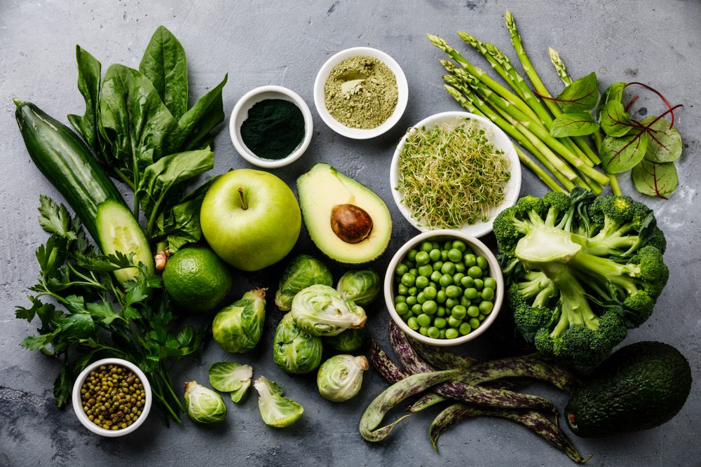 Healthy Green food Clean eating selection Protein source for vegetarians: avocado, asparagus, apple, broccoli, spinach, spirulina, green peas on gray concrete background