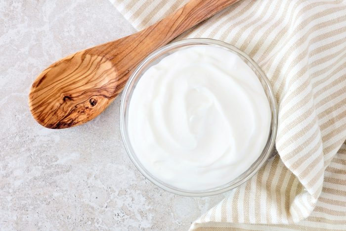 Greek yogurt in a bowl, downward view with cloth and spoon on a white marble