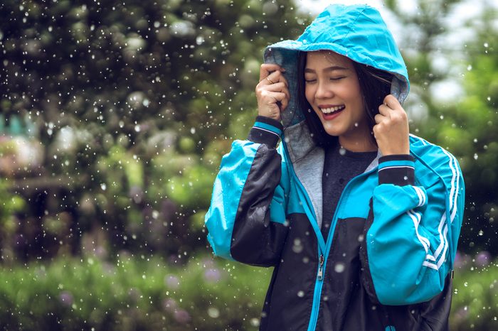 Asian woman wearing a raincoat outdoors. She is happy.