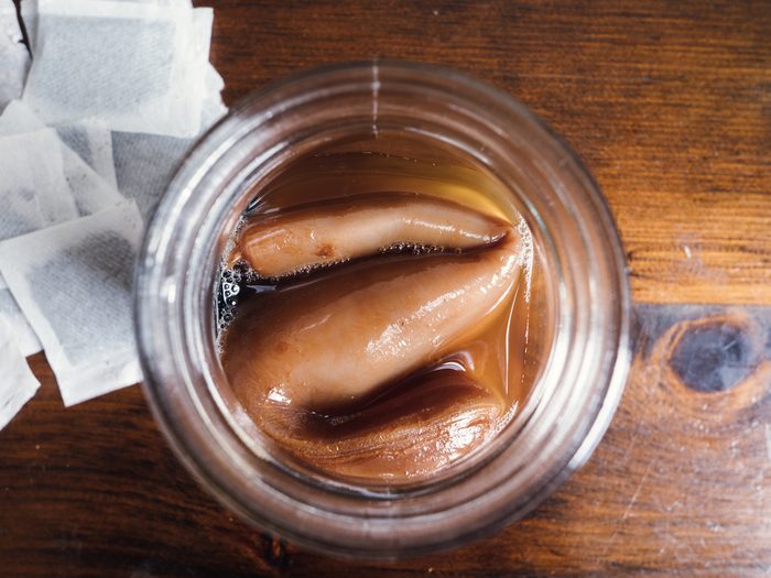 Jar of starter tea for Kombucha tea. SCOBY with tea bags on rustic wood table. Closeup.