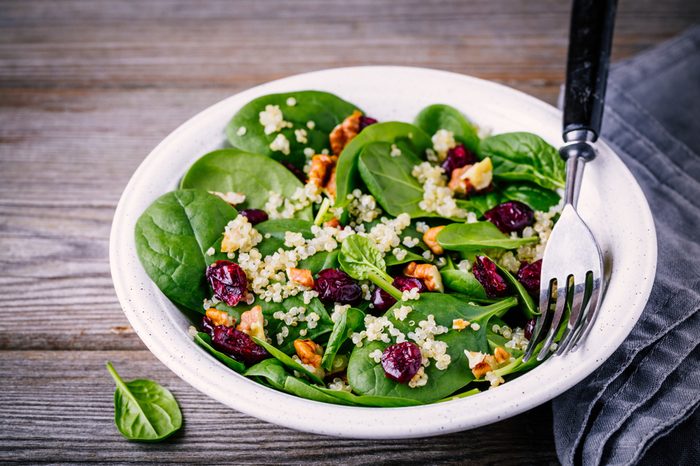 Sinach, quinoa, walnuts and dried cranberries in a bowl on wooden background