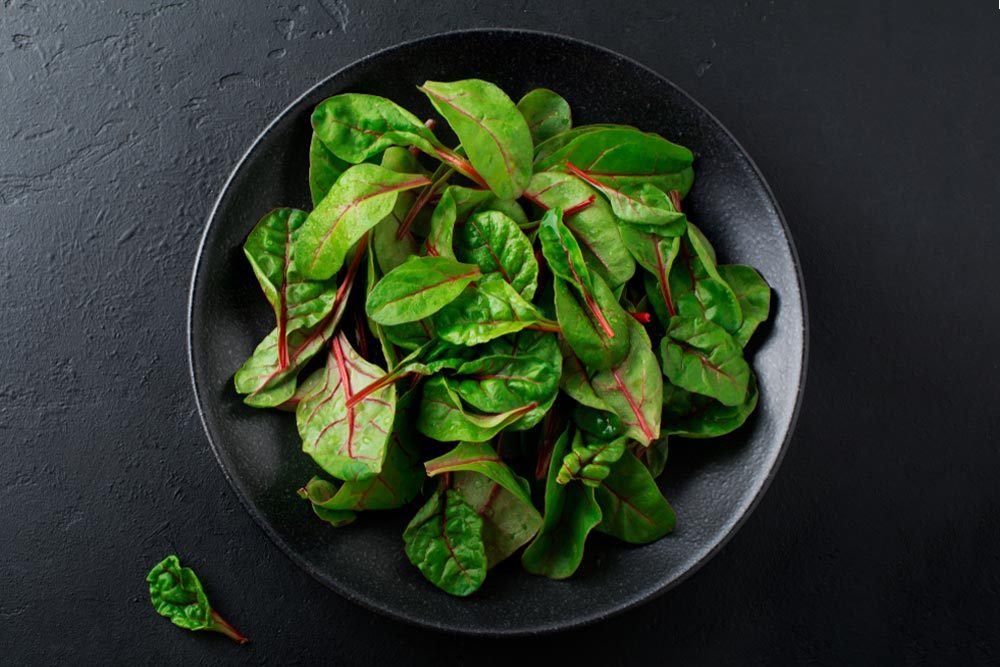 Fresh young leaves of chard for salad in a dark ceramic dish on black concrete background. Selective focus. Copy space. Top view.