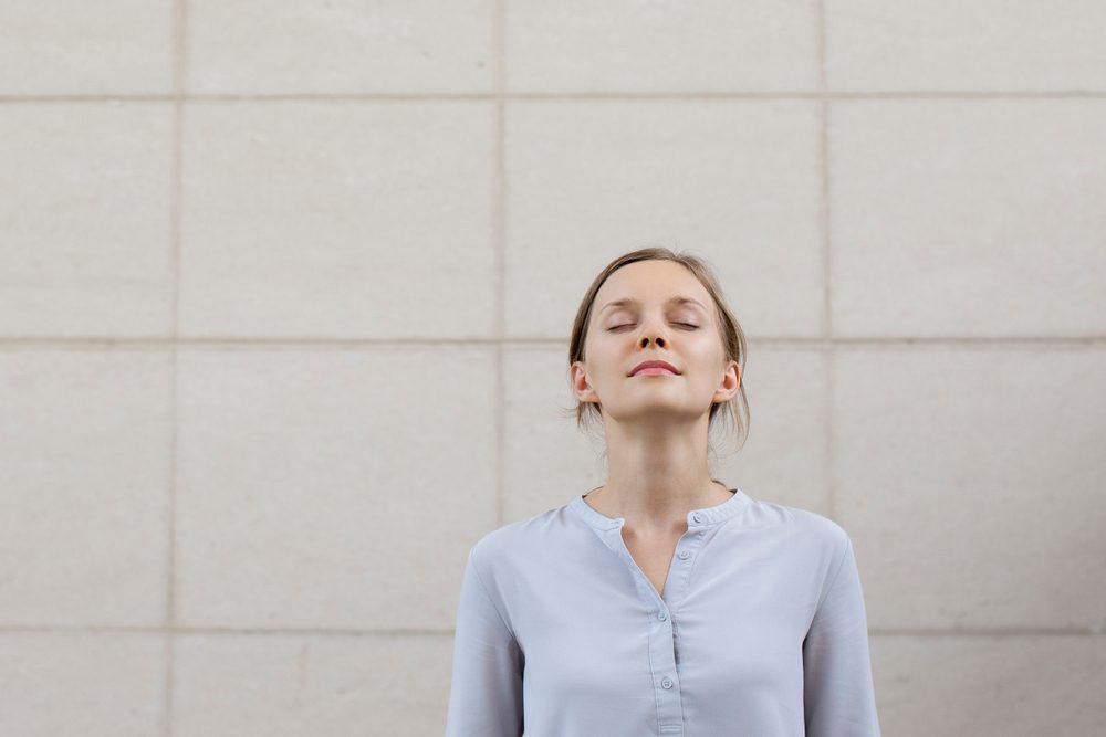 woman with eyes closed, relaxing against a wall
