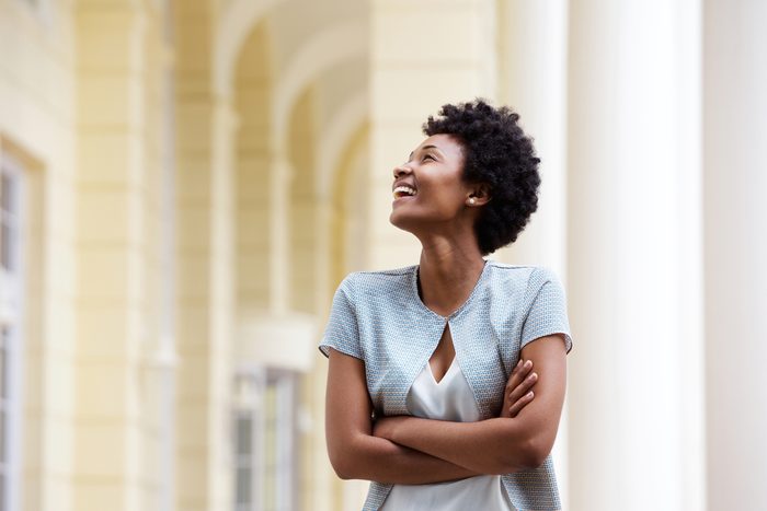 Portrait of a smiling young african woman standing outdoors with her arms crossed and looking away