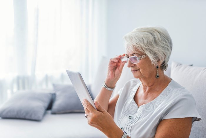 Grandma learning tablet. Senior woman reading a message, e-book or information on her tablet computer with a look of excited anticipation as she sits on a couch at home