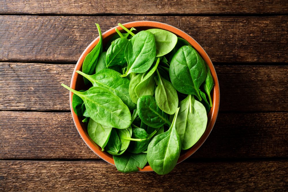 Fresh spinach leaves in bowl on rustic wooden table. Top view.