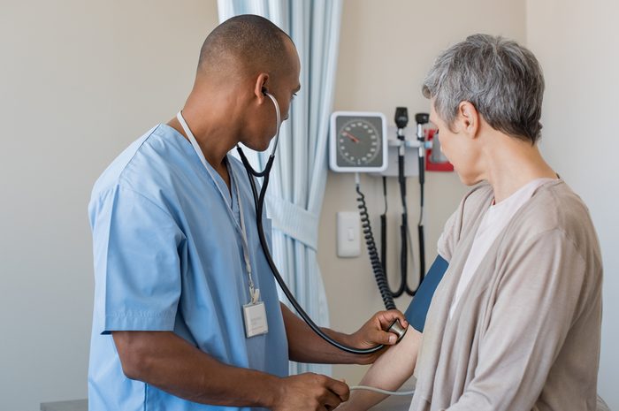 Male nurse checking blood pressure of a senior woman in medical office. African doctor taking the blood pressure of his patient at hospital. Young doctor measuring the blood pressure of mature woman.