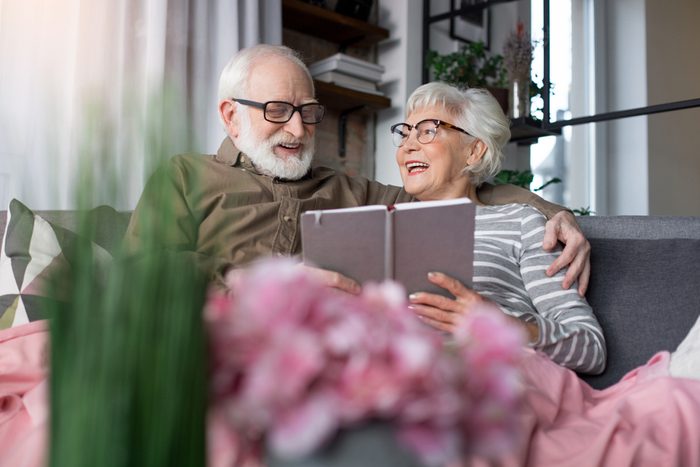 Pleasant memories. Portrait of old charming couple remembering sweet moments. Woman is looking at husband while laughing. Man is regarding at picture while tenderly cuddling wife