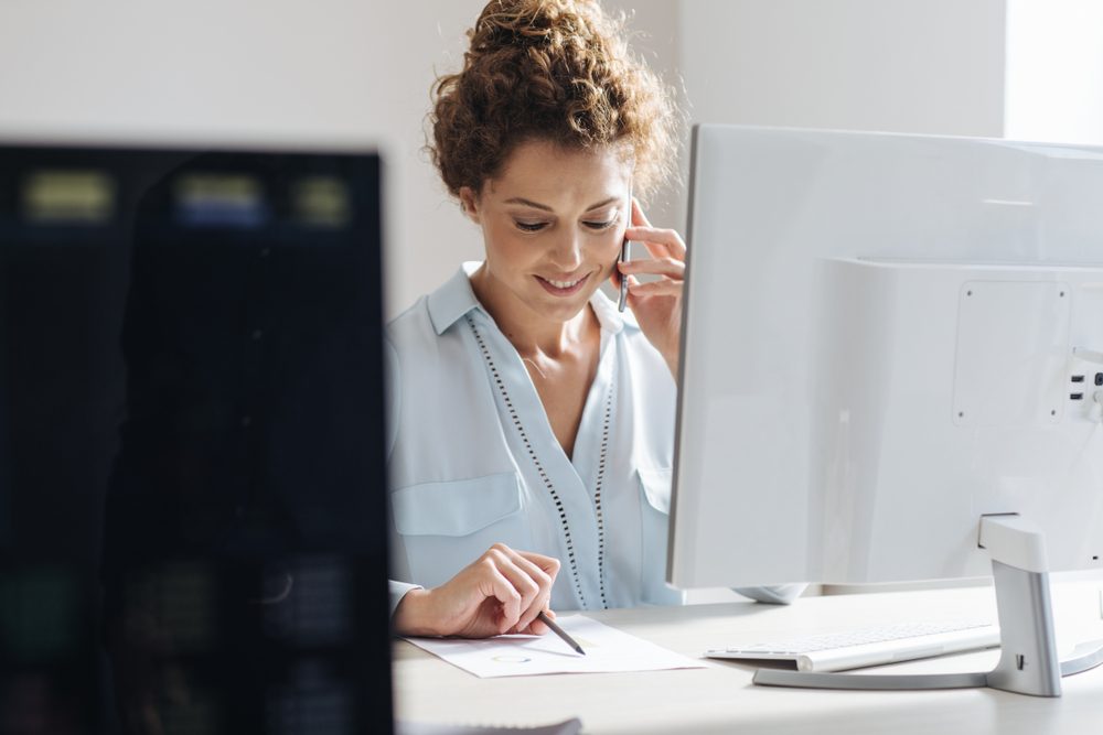 Young businesswoman using a mobile phone while working on a desktop computer