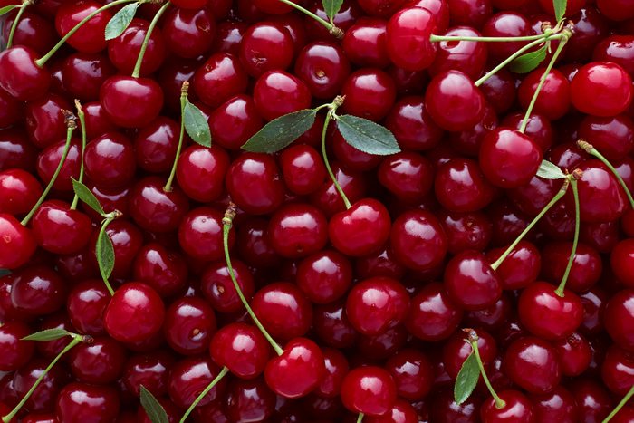 Close up of pile of ripe cherries with stalks and leaves. Large collection of fresh red cherries. Ripe cherries background.