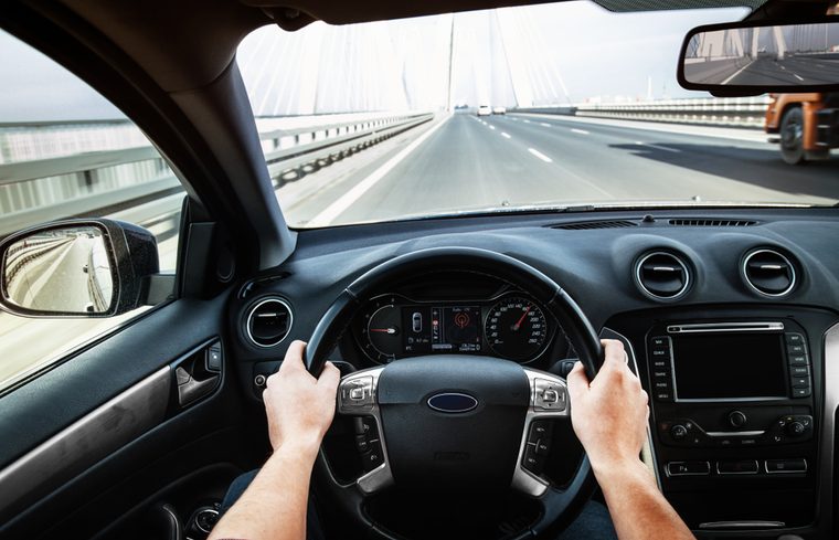 Person driving a car on a highway, hands on steering wheel