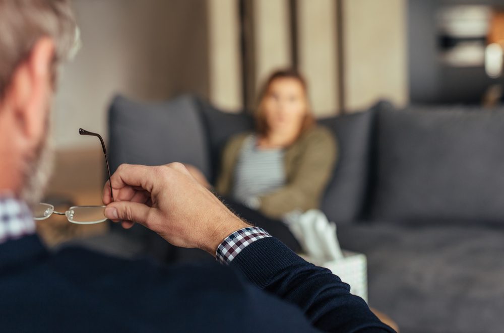 Hands of psychologist holding glasses and listening to woman during therapy session