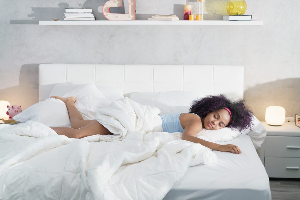 Young African American woman waking up at home. Portrait of happy black girl smiling, enjoying a large king size mattress all for herself.