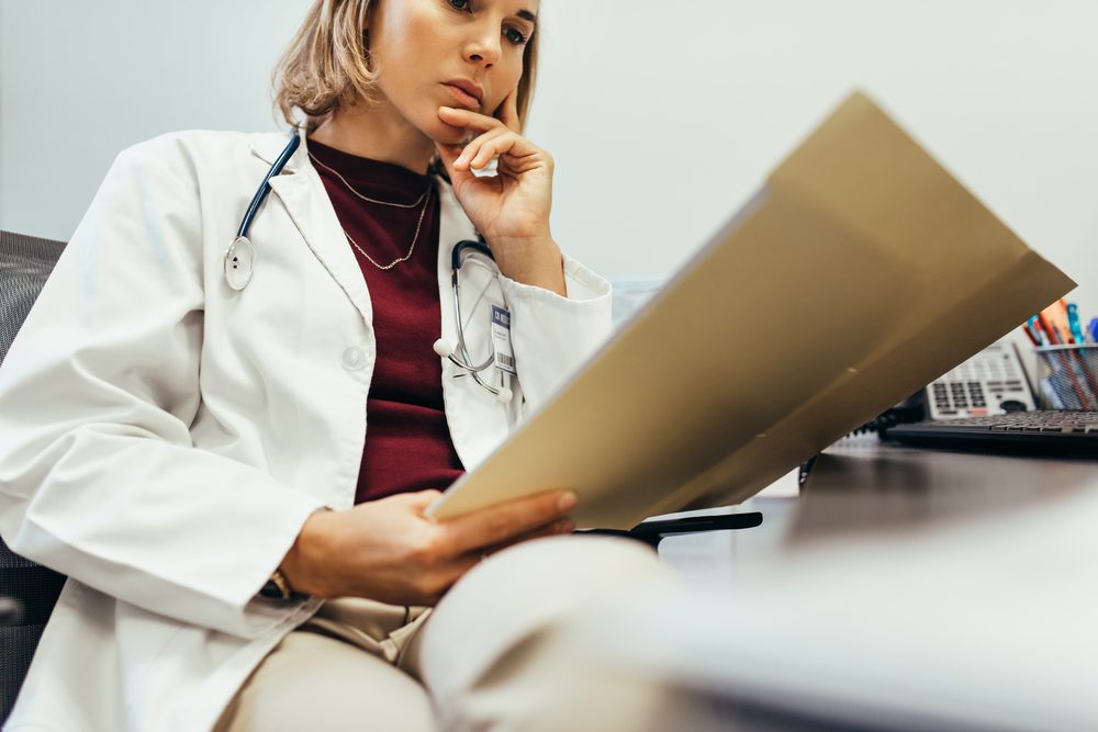 Doctor reading medical documentation in hospital. Female physician sitting in her office and examining medical records.