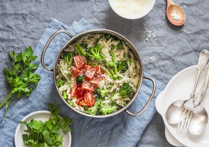 One pot orzo primavera. Orzo pasta with asparagus, broccoli, green peas and cream in a saucepan. On a light background, top view
