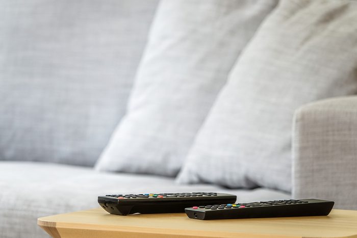 Interior of sunny TV room with remote controls set on a wooden table. Gray sofa in the background. Copy space