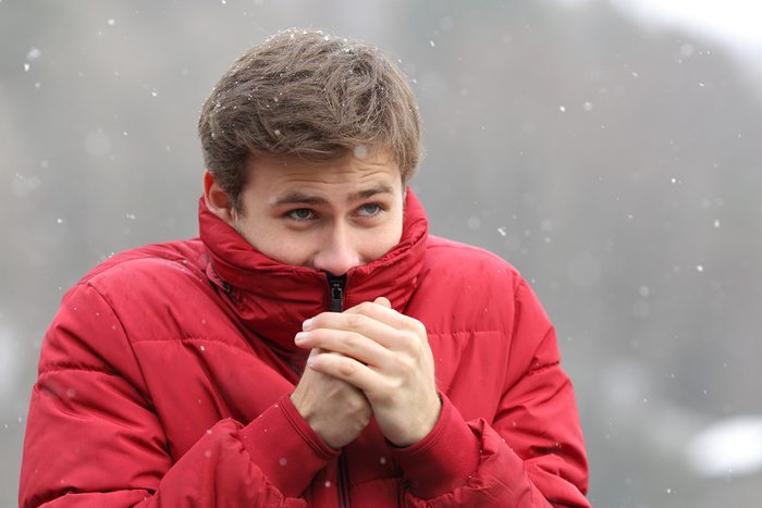 Man shivering in cold winter and rubbing hands while is snowing