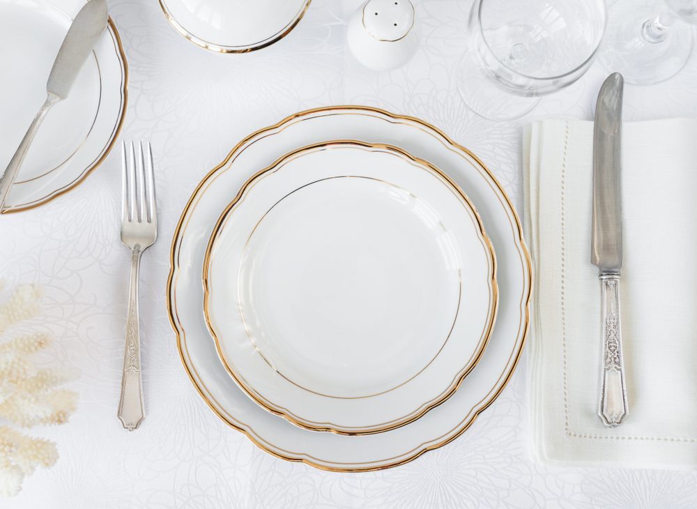 Beautifully decorated table with white plates, glasses, antique cutlery and white coral on luxurious tablecloths