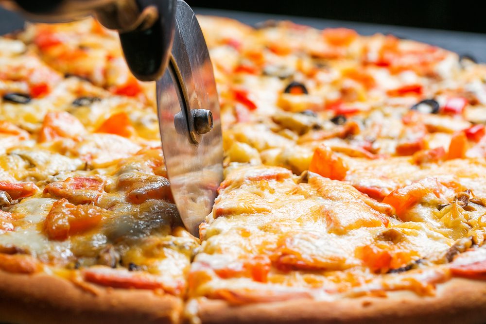 Closeup hand of chef baker in white uniform cutting pizza at kitchen